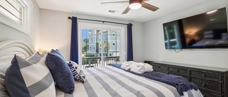 A bedroom with a bed, a ceiling fan, a TV, and a view of buildings outside.