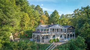 Une grande maison à deux étages, dotée d’une terrasse et entourée d’une forêt dense.