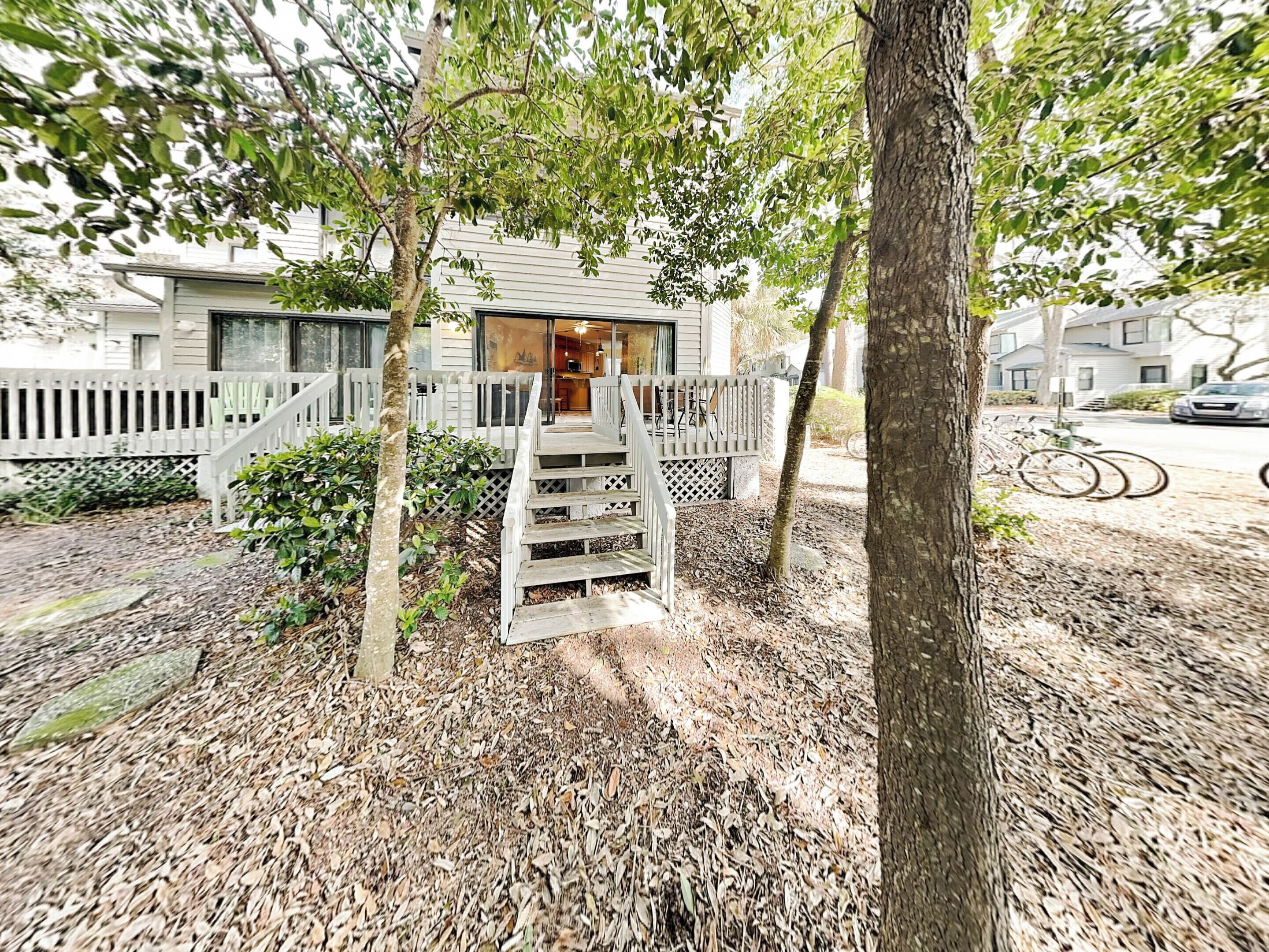 A wooden deck with a staircase leading to a house, surrounded by trees and a wooden fence.
