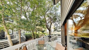 Un balcon vitré, agrémenté d’une table et de chaises, entouré d’arbres et délimité par une clôture blanche.