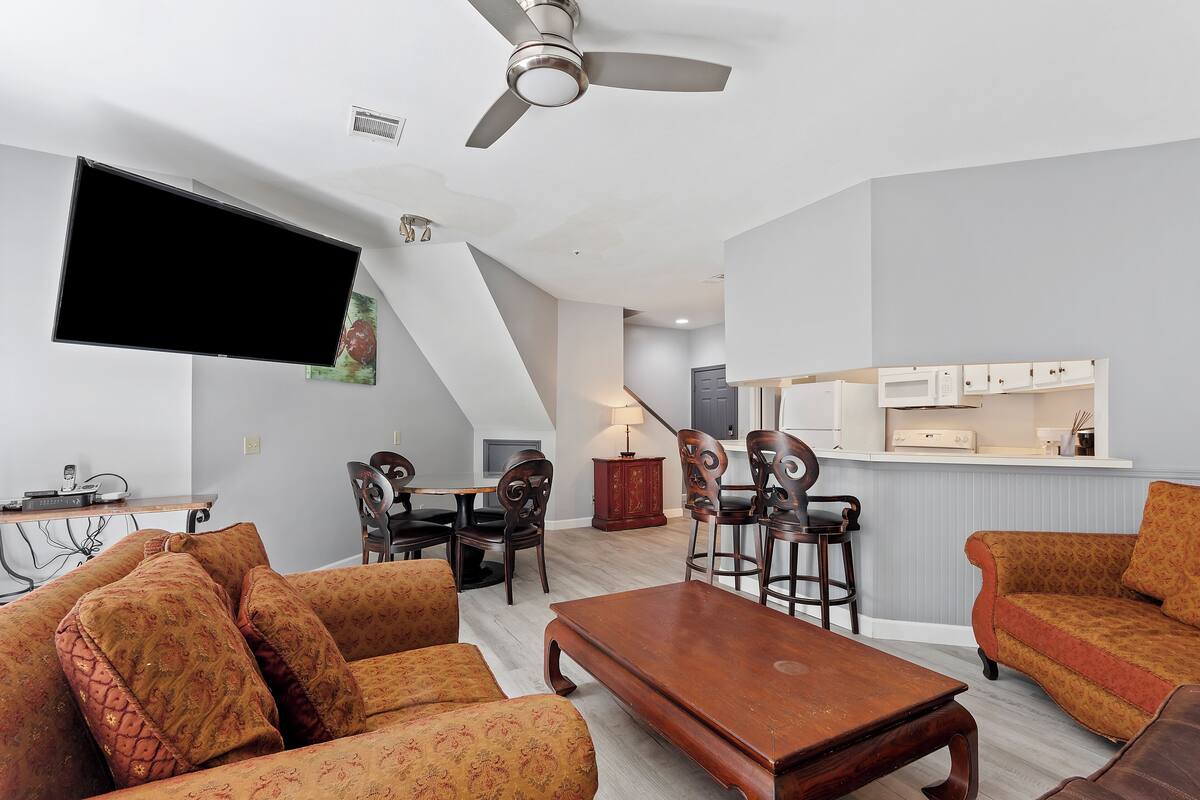 A living room with a flat-screen TV, a ceiling fan, and a dining area with a table and chairs.