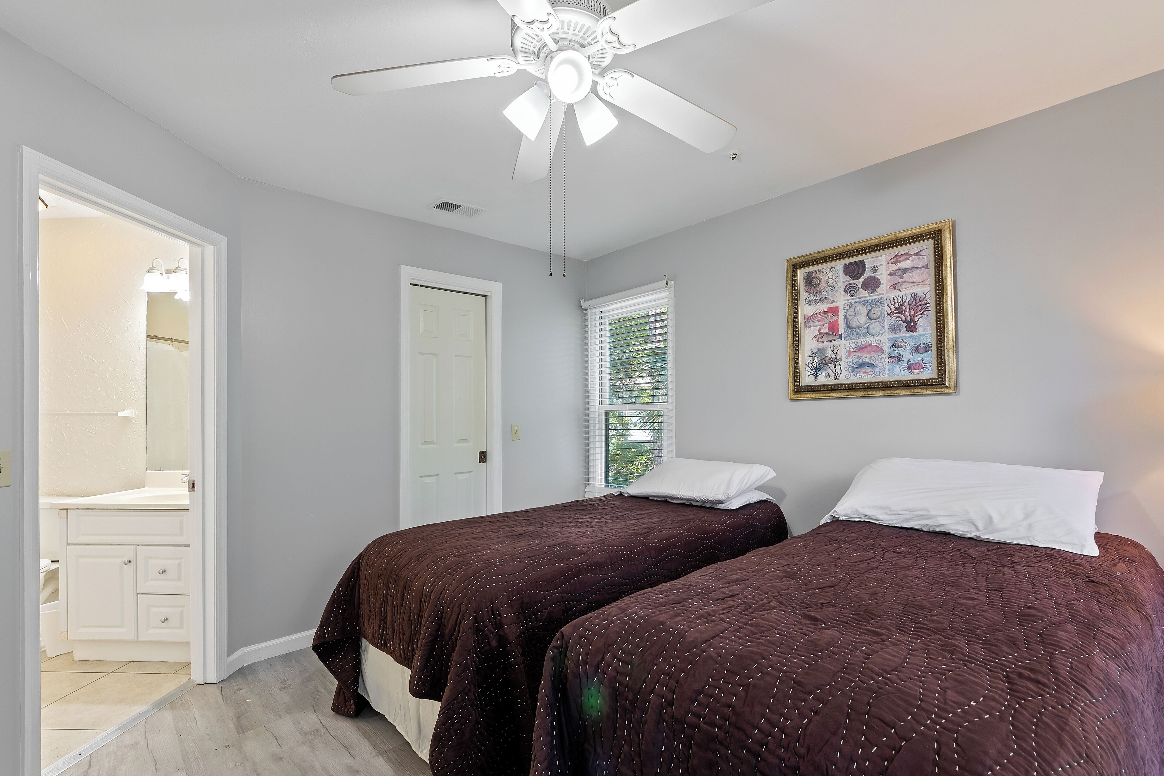 Une chambre avec deux lits, un ventilateur de plafond, une porte et une fenêtre avec des stores.