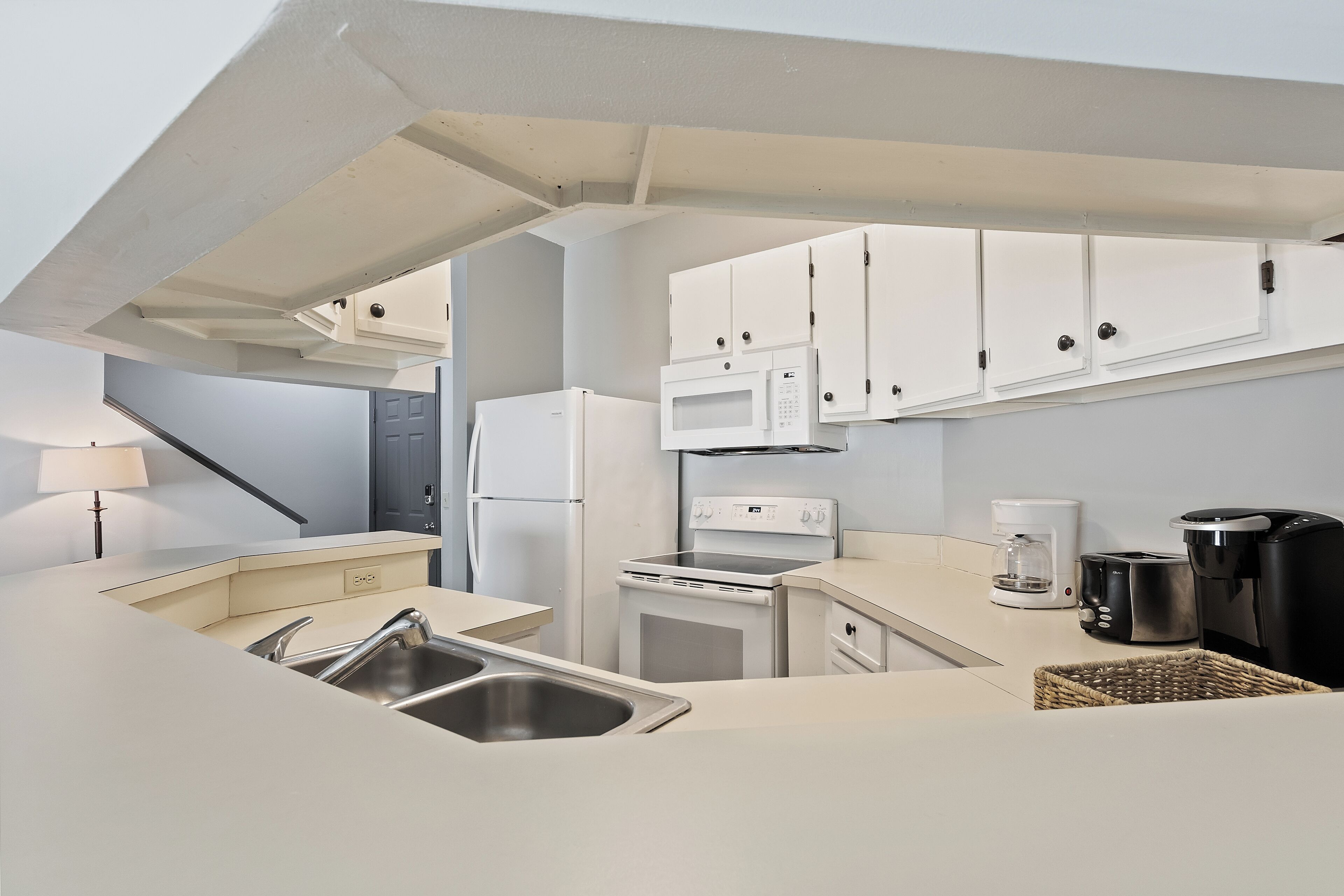 Una cocina compacta con armarios blancos, un microondas integrado, una estufa, una cafetera y un tostador.