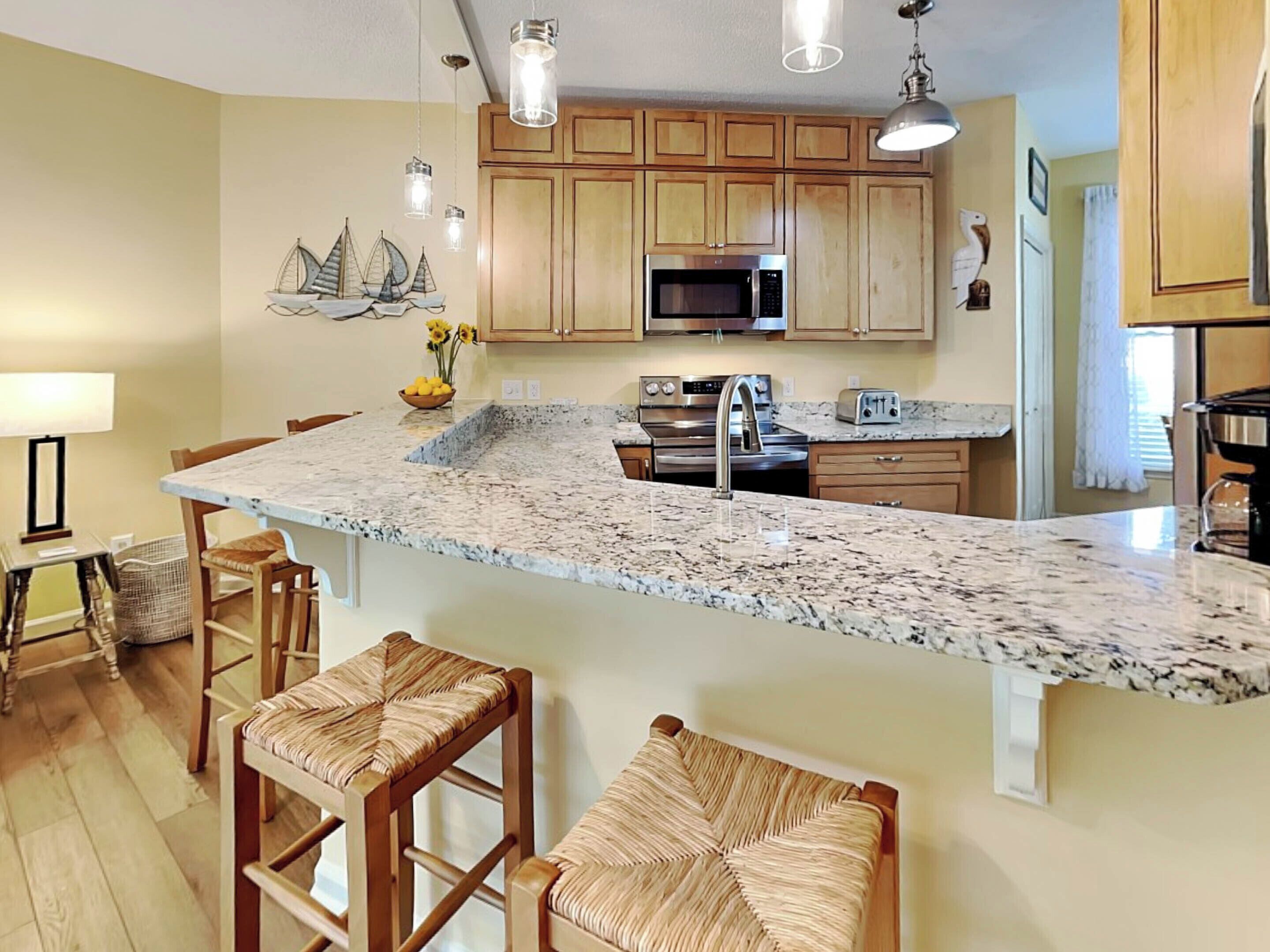 A kitchen with wooden cabinets, a granite countertop, stainless steel appliances, and a bar area with wicker stools.