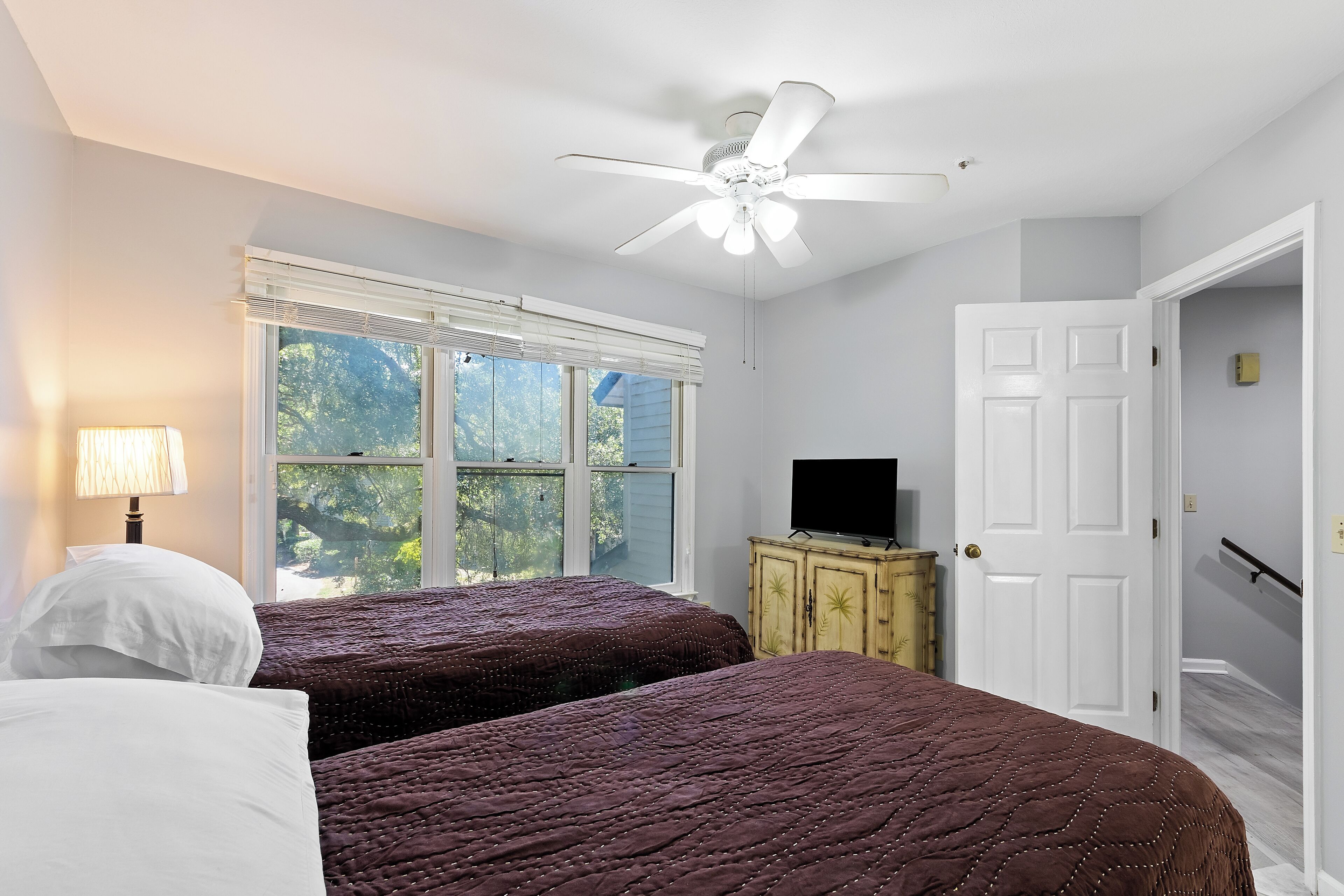 A bedroom with two beds, a ceiling fan, a television, and a window with blinds.