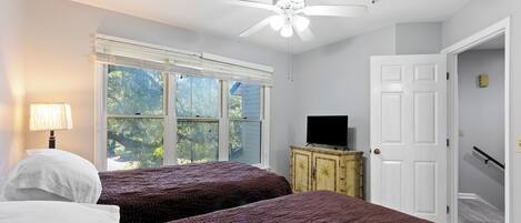 A bedroom with two beds, a ceiling fan, a television, and a window with blinds.