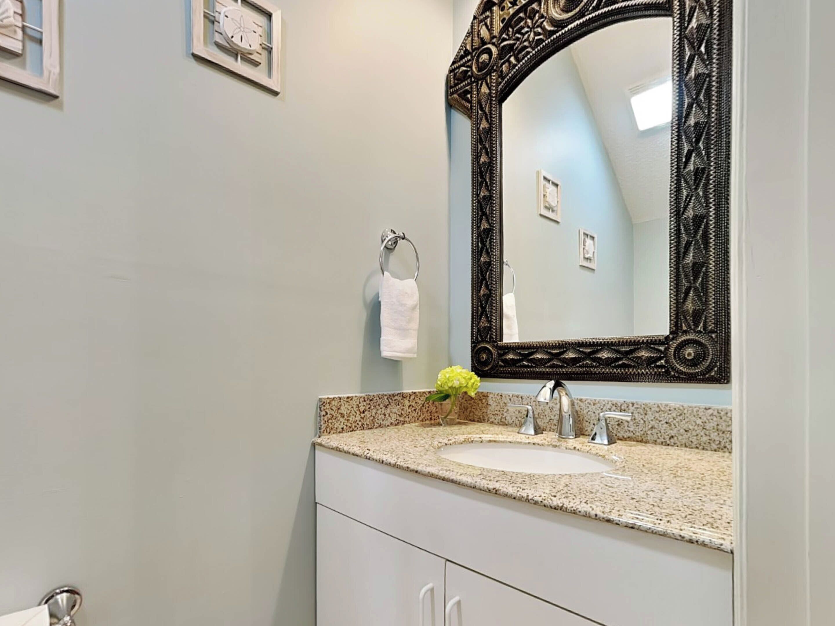 A bathroom with a granite countertop, a sink, a mirror with an ornate frame, and a towel rack with a white towel.