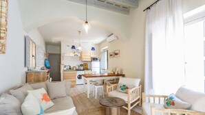 Amplia sala de estar con un conjunto de sofás, una mesa redonda de centro y una mesa de comedor con sillas. Se observa una cocina al fondo con un microondas y un lavamanos.