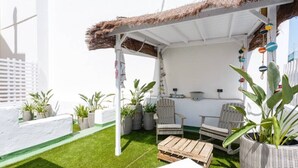 Un área de estar al aire libre techada, con mobiliario de mimbre y plantas en macetas.