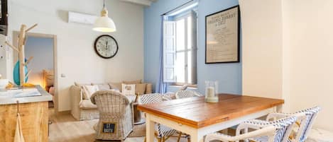 A cozy dining area with a wooden table and wicker chairs, a clock on the wall, and a framed menu on the wall.