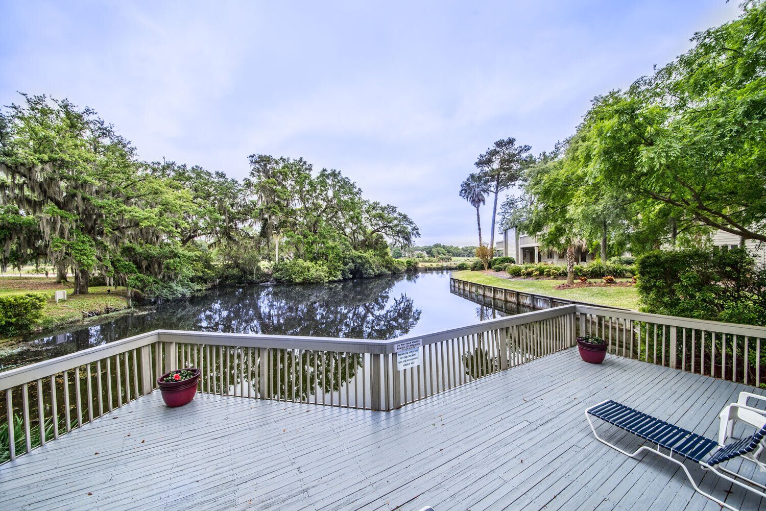 A wooden deck with a view of a calm water body, surrounded by lush greenery and trees.