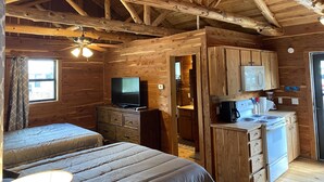 A wooden cabin with a kitchen area, a television, and two beds. - Charming Cabin on the San Marcos River with large back screened-in deck! - L2 (Kingsbury)