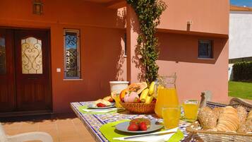 An outdoor dining area with a table set for breakfast, including fruits, bread, and a pitcher of juice.