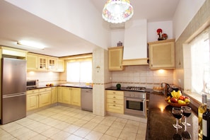 A kitchen with wooden cabinets, a stainless steel refrigerator, a dishwasher, an oven, and a sink. There is a fruit bowl on the counter and a bottle of wine.