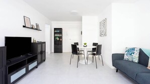 A modern living room with a flat-screen TV, a black entertainment unit, a dining table with chairs, and a grey sofa with a decorative pillow. - Home2Book Paradise Los Cristianos, Pool & Wifi (Los Cristianos)