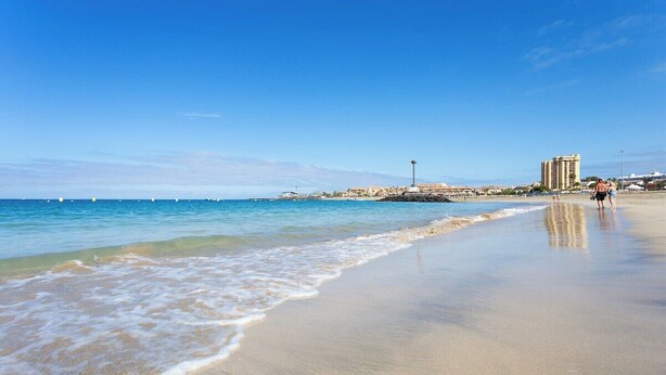 A beach with clear blue water, a sandy shore, and buildings in the background. - Home2Book Paradise Los Cristianos, Pool & Wifi (Los Cristianos)