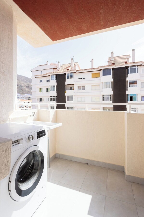 A balcony with a washing machine, a sink, and a view of residential buildings.