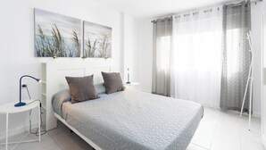 A modern bedroom with a large bed, two wall-mounted paintings, a bedside table with a lamp, and sheer curtains on the window. - Home2Book Paradise Los Cristianos, Pool & Wifi (Los Cristianos)