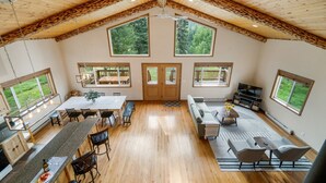A spacious room with a high ceiling, wooden beams, large windows, a dining area, a seating area, and a television. - Welcome to Lemon Lodge! Relax and unwind in this private and secluded cabin.  (Durango)