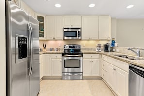 A modern kitchen with stainless steel appliances, beige cabinetry, and a granite countertop.
