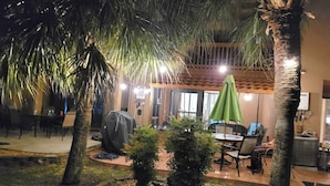 Un espace extérieur aménagé avec des tables et des chaises, entouré de palmiers et protégé par des parasols.