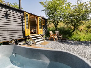 A wooden cabin with a hot tub, outdoor seating, and a gravel path leading to the entrance. - Moelfre - Shepherds Hut (Llanbedr)