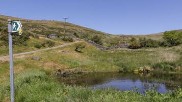 A rural landscape with a walking trail sign, a stone wall, a small pond, and a stone house in the background.