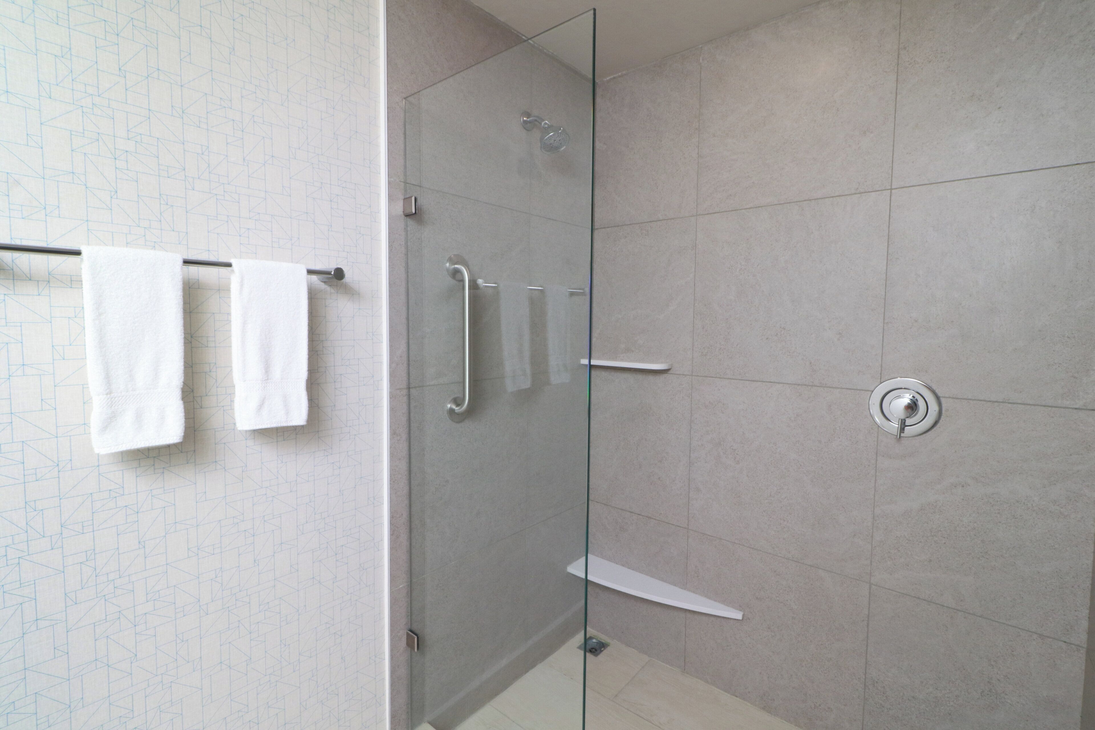 Un baño moderno con cabina de ducha de vidrio, un perchero con dos toallas y un inodoro fijado a la pared.
