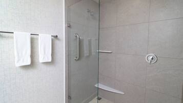 Un baño moderno con cabina de ducha de vidrio, un perchero con dos toallas y un inodoro fijado a la pared.