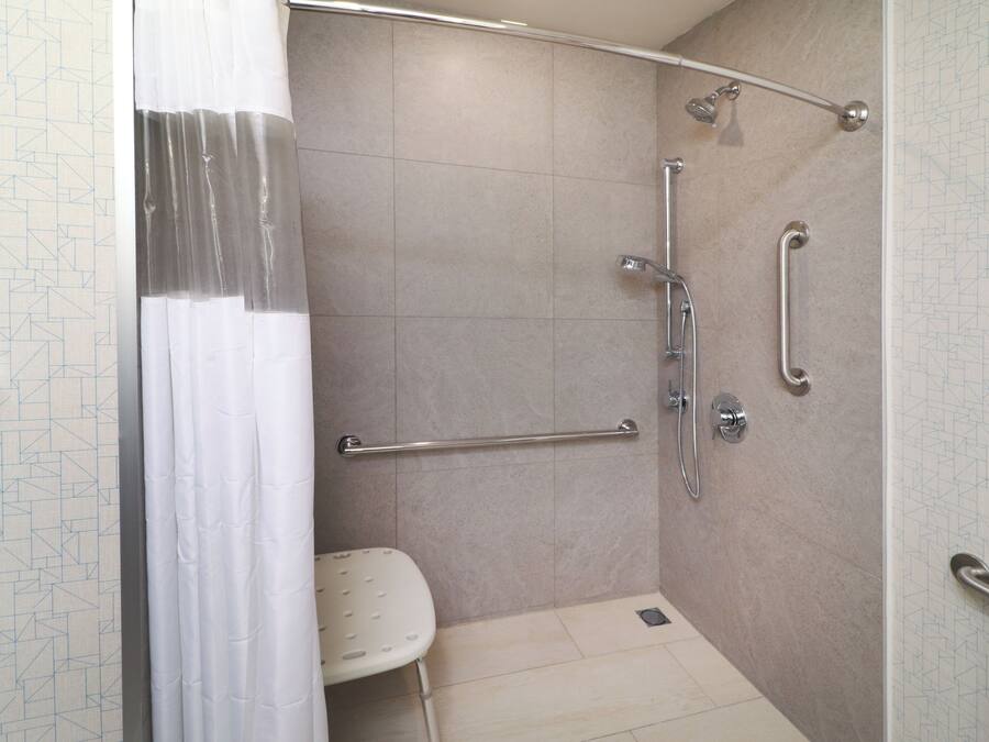 Área de chuveiro com barra de apoio, chuveiro manual e vaso sanitário.