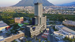 A high-rise building with multiple floors, surrounded by a cityscape and mountains in the background. - Holiday Inn Express Monterrey Fundidora by IHG (Monterrey)