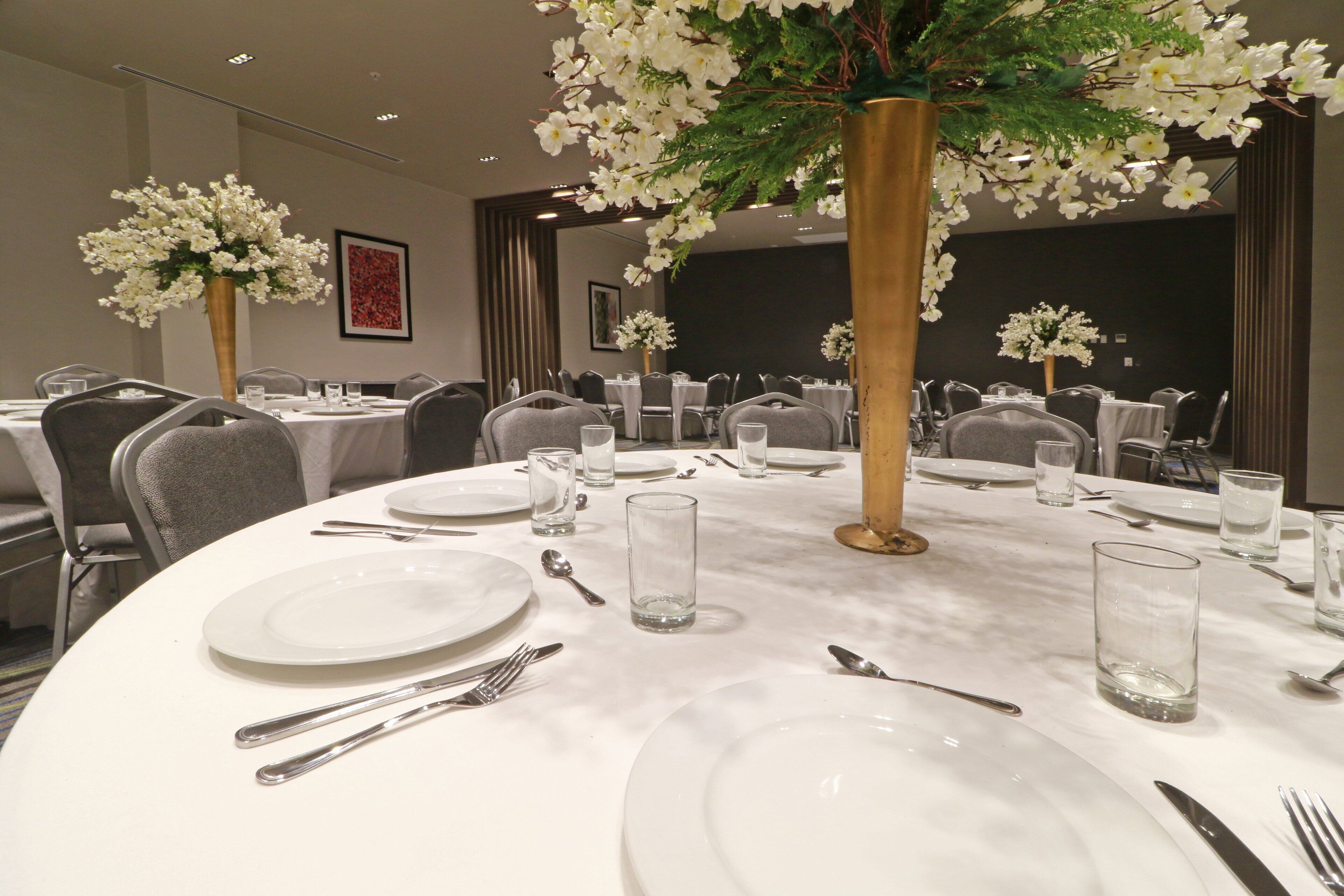 A conference room with round tables, white tablecloths, and floral centerpieces.