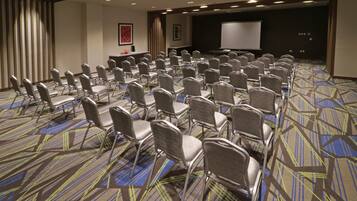 Un salón de conferencias con filas de sillas, un escenario con una pantalla y una alfombra estampada.