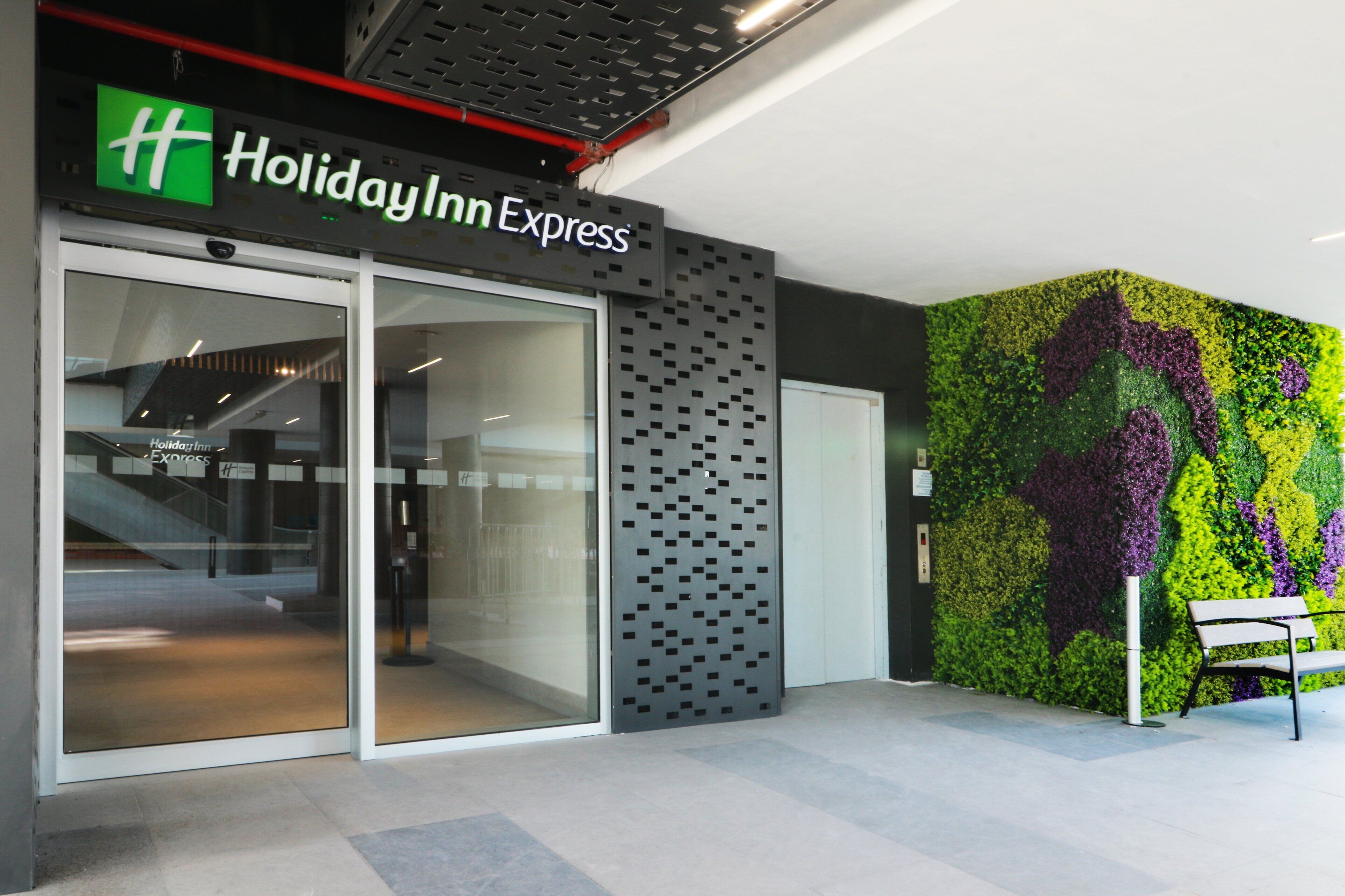 Un Holiday Inn Express amb una entrada moderna, una porta de vidre i un mural de paret colorit.