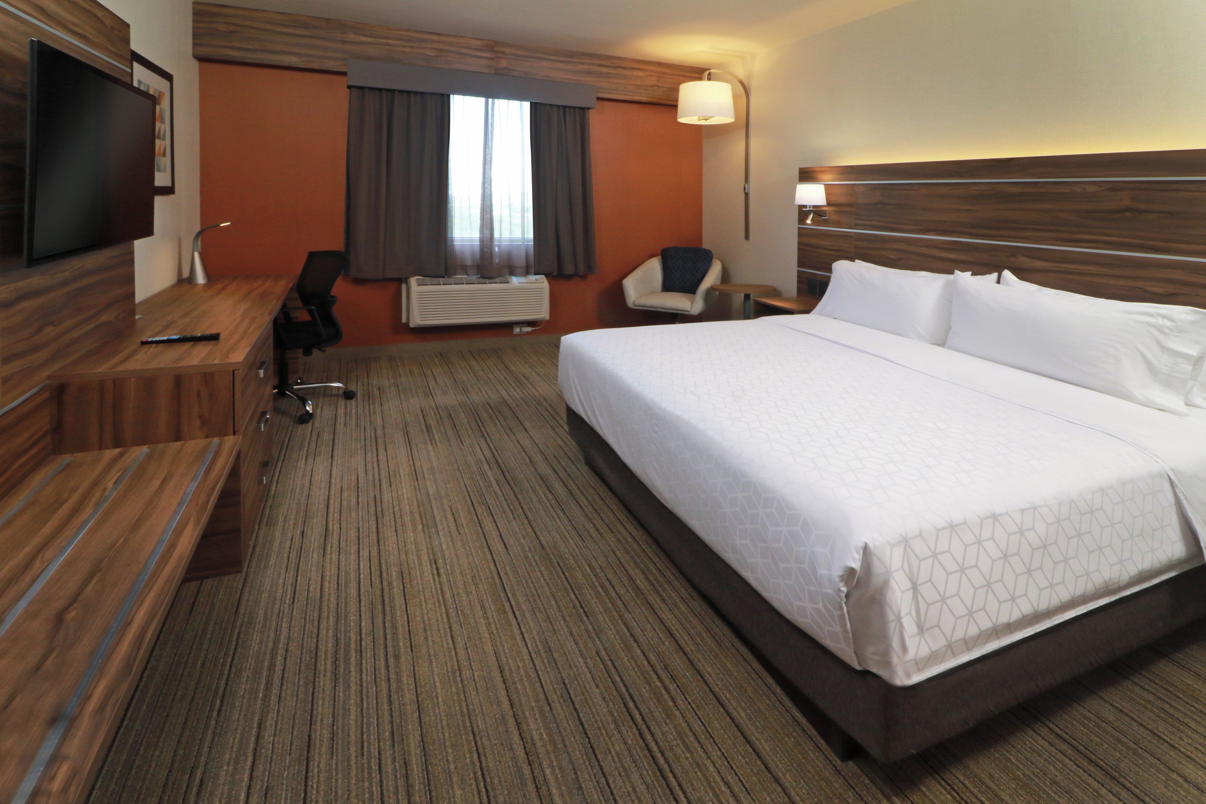 Habitación de hotel con una cama grande, un escritorio, una silla, un televisor y una ventana con cortinas.