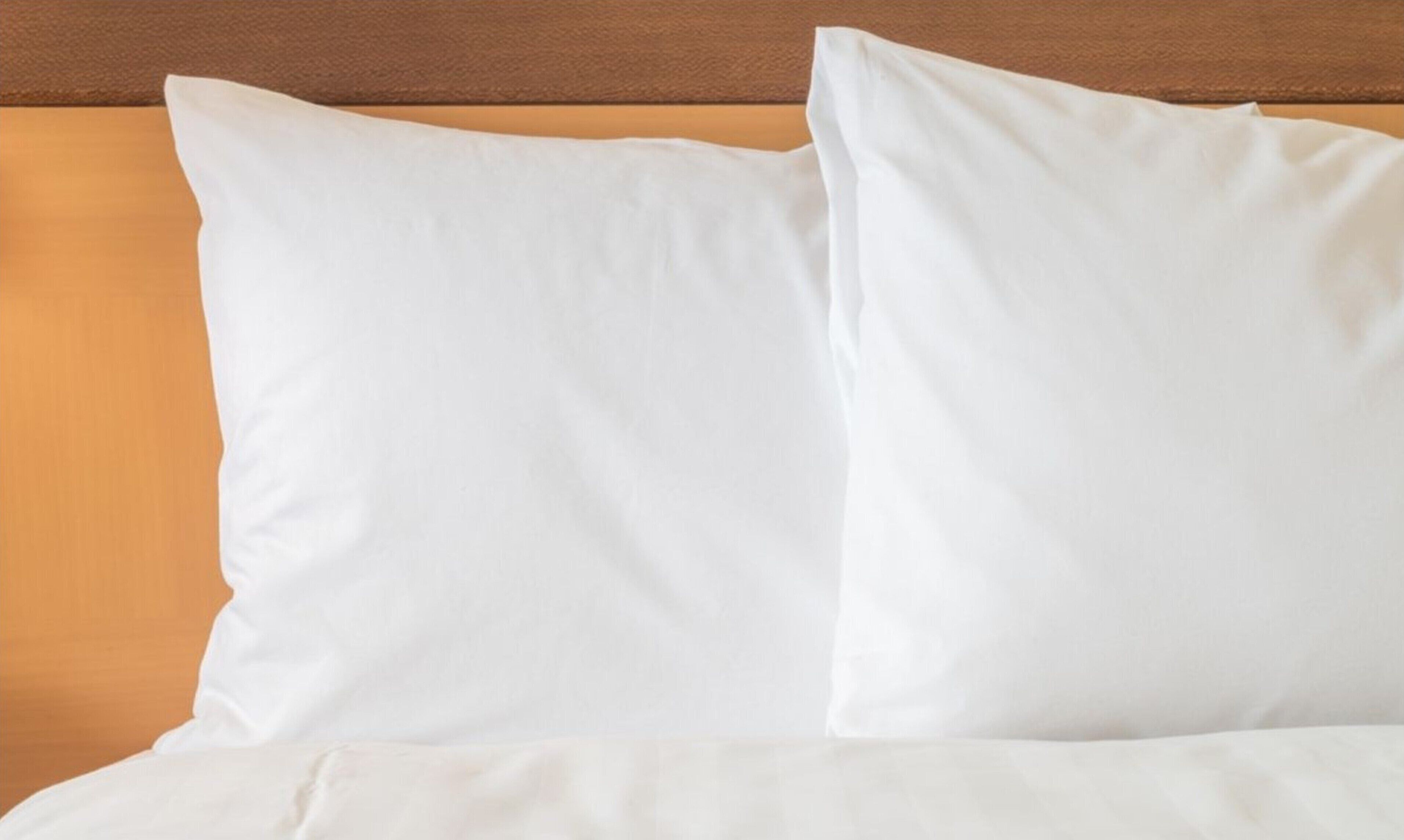 Una cama con ropa de cama y almohadas blancas, apoyada en un cabecero de madera.