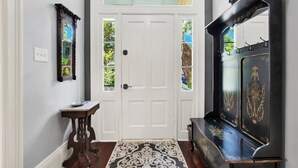A hallway with a white door, a small table with a decorative mirror, and a black piano with gold detailing. - Charmer near Forsyth Park, Heated Pool Access! (Savannah)