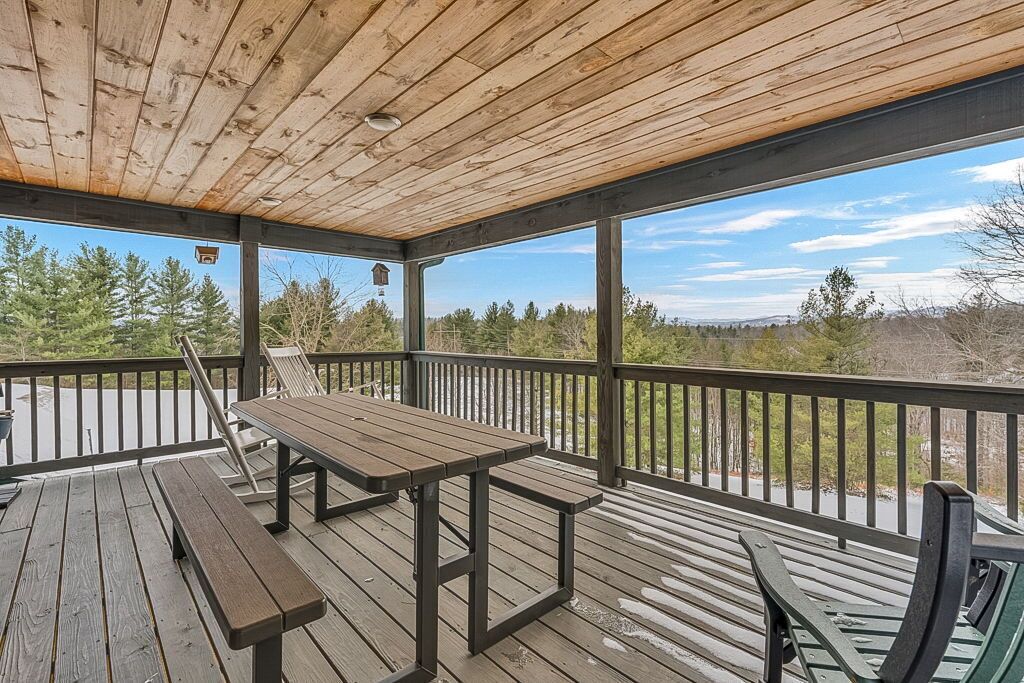 Une terrasse couverte, dotée d’une table et de bancs en bois, qui offre une vue sur un paysage naturel.