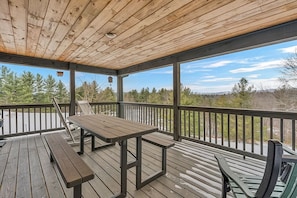 A covered deck with a wooden table and benches, overlooking a natural landscape.