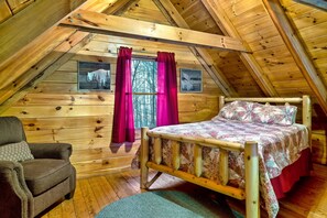 Une chambre mansardée chaleureuse avec un plafond en bois, un lit, une chaise et deux tableaux encadrés au mur.