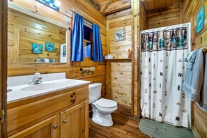 Une salle de bain rustique, avec des murs en bois, un lavabo blanc, des toilettes et un rideau de douche orné de motifs animaliers.