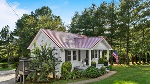A white house with a metal roof, a front porch, and a flag.