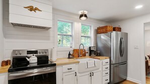 A modern kitchen with white cabinetry, a stainless steel refrigerator, a built-in oven, and a wooden countertop.