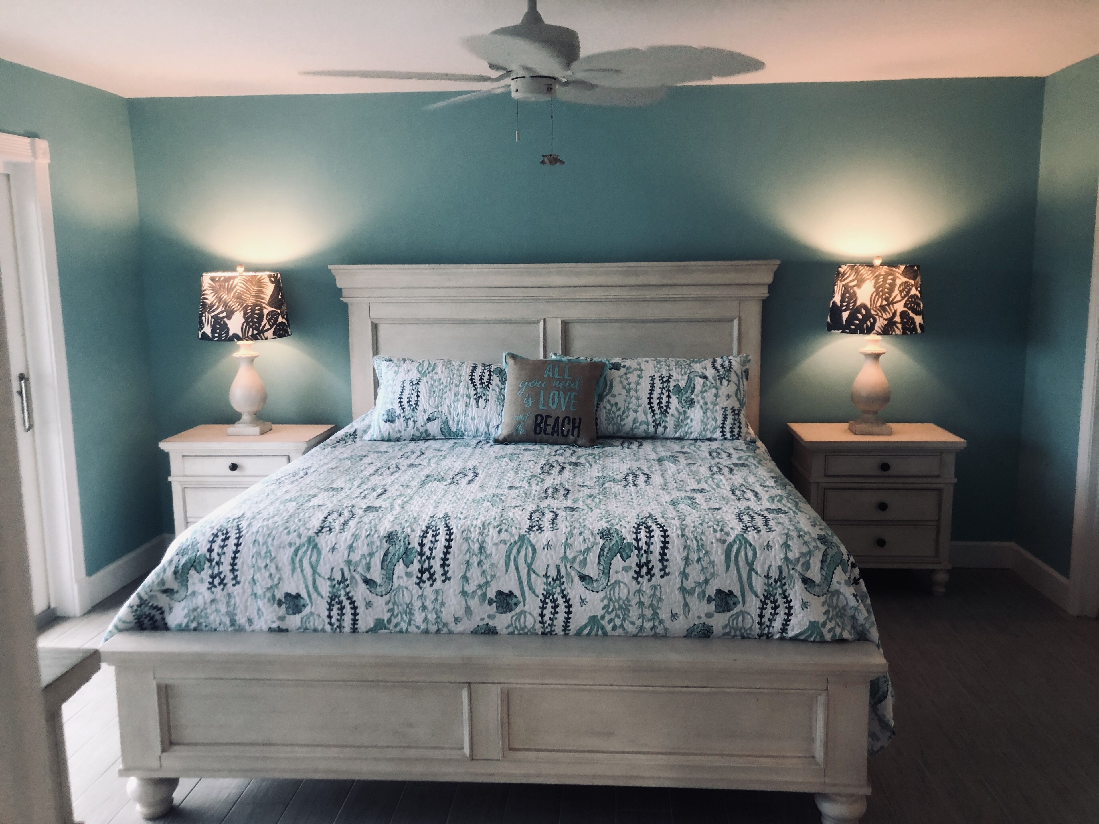 A bedroom with a bed, two bedside tables, a ceiling fan, and two wall-mounted lamps.