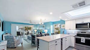 A modern kitchen with white cabinets, a large island, and a dining area with blue chairs and a table. - Beautiful bright, updated 2 bedroom, 2 bath oceanfront condo spectacular views! (Stuart)