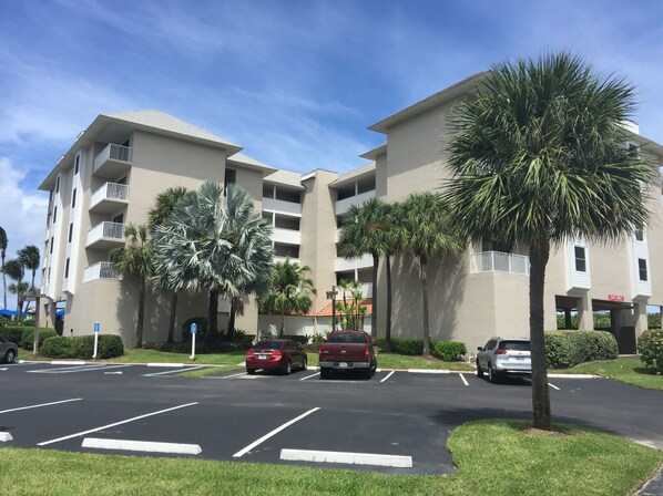 A multi-story hotel with a parking lot, palm trees, and a clear blue sky.