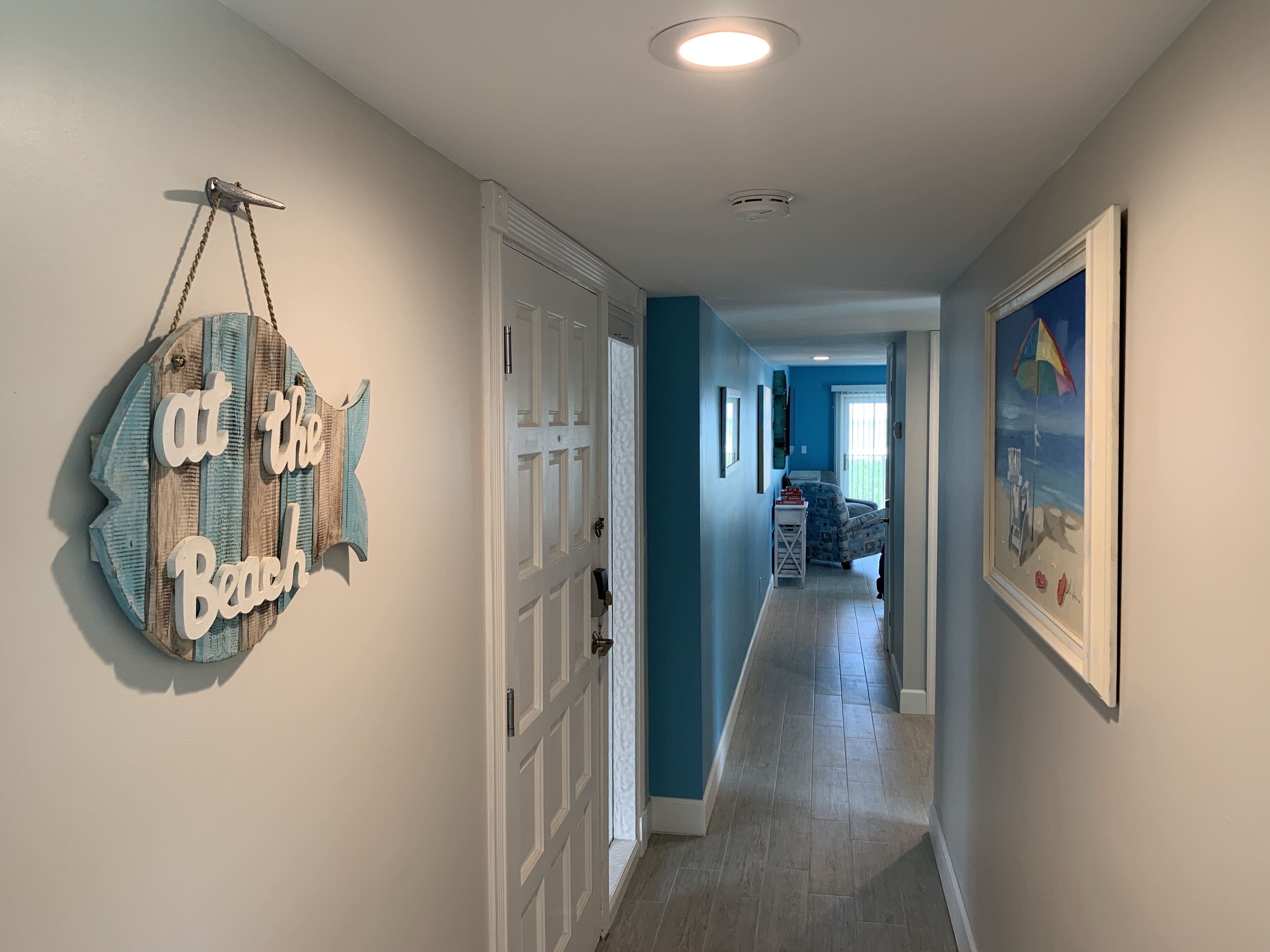 A hallway with a sign reading "at the Beach," a door, and a framed picture on the wall.