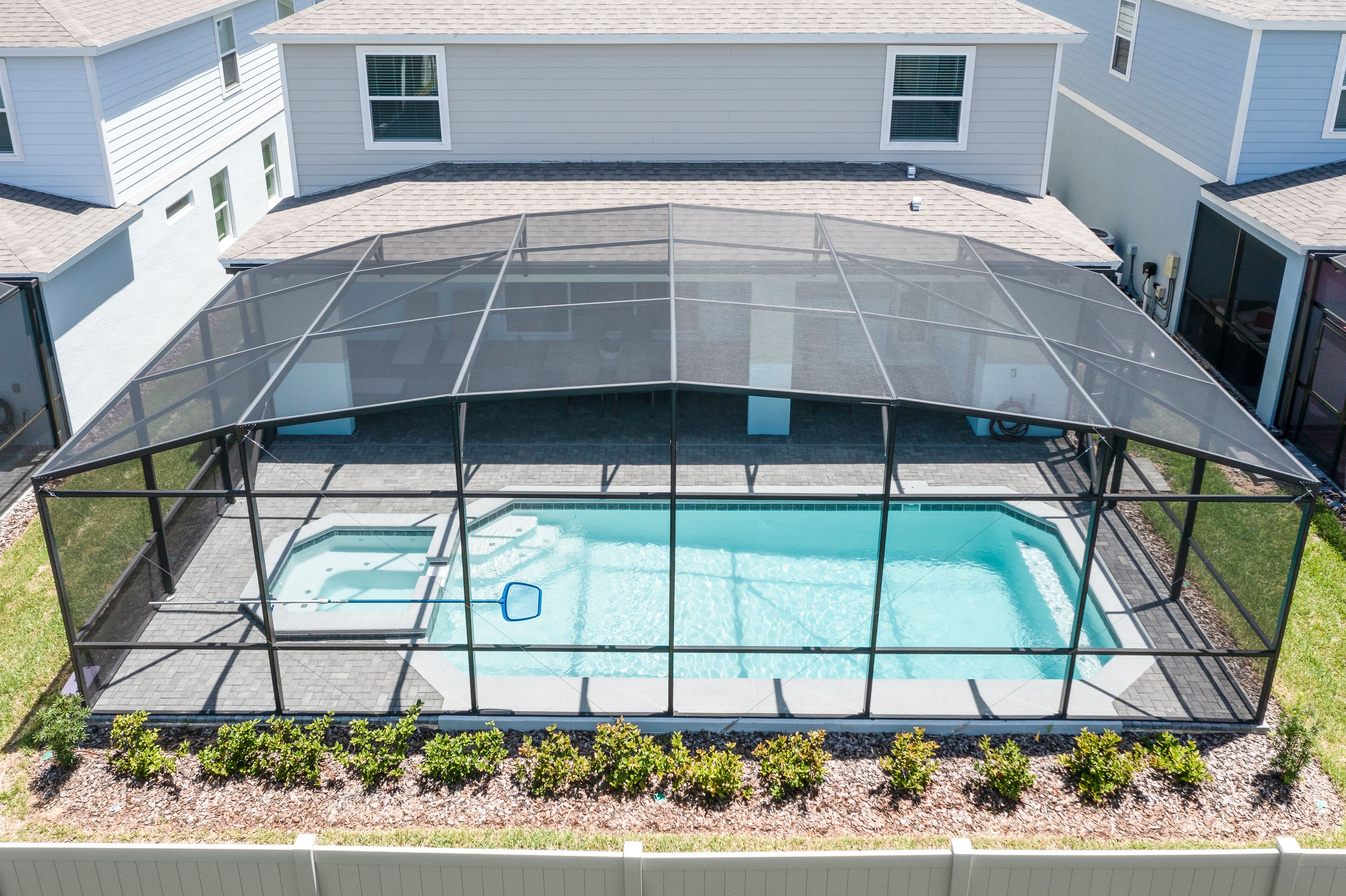 A swimming pool with a glass enclosure, surrounded by a brick deck and a small garden area.