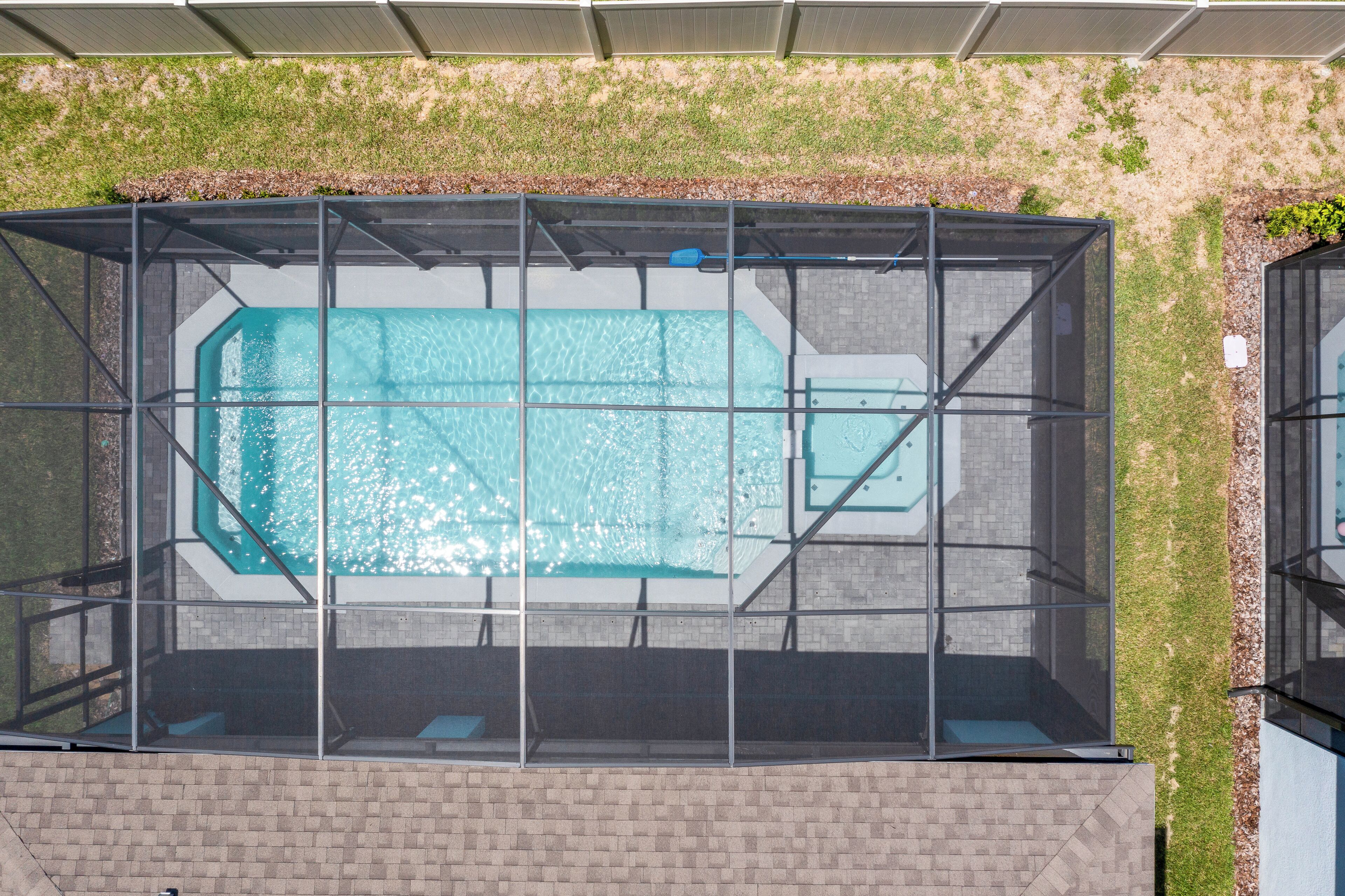 A rooftop swimming pool with a glass enclosure, surrounded by a brick wall and a grassy area.