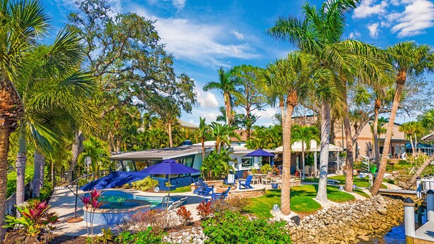 A resort with a swimming pool, lounge chairs, palm trees, and a modern house.